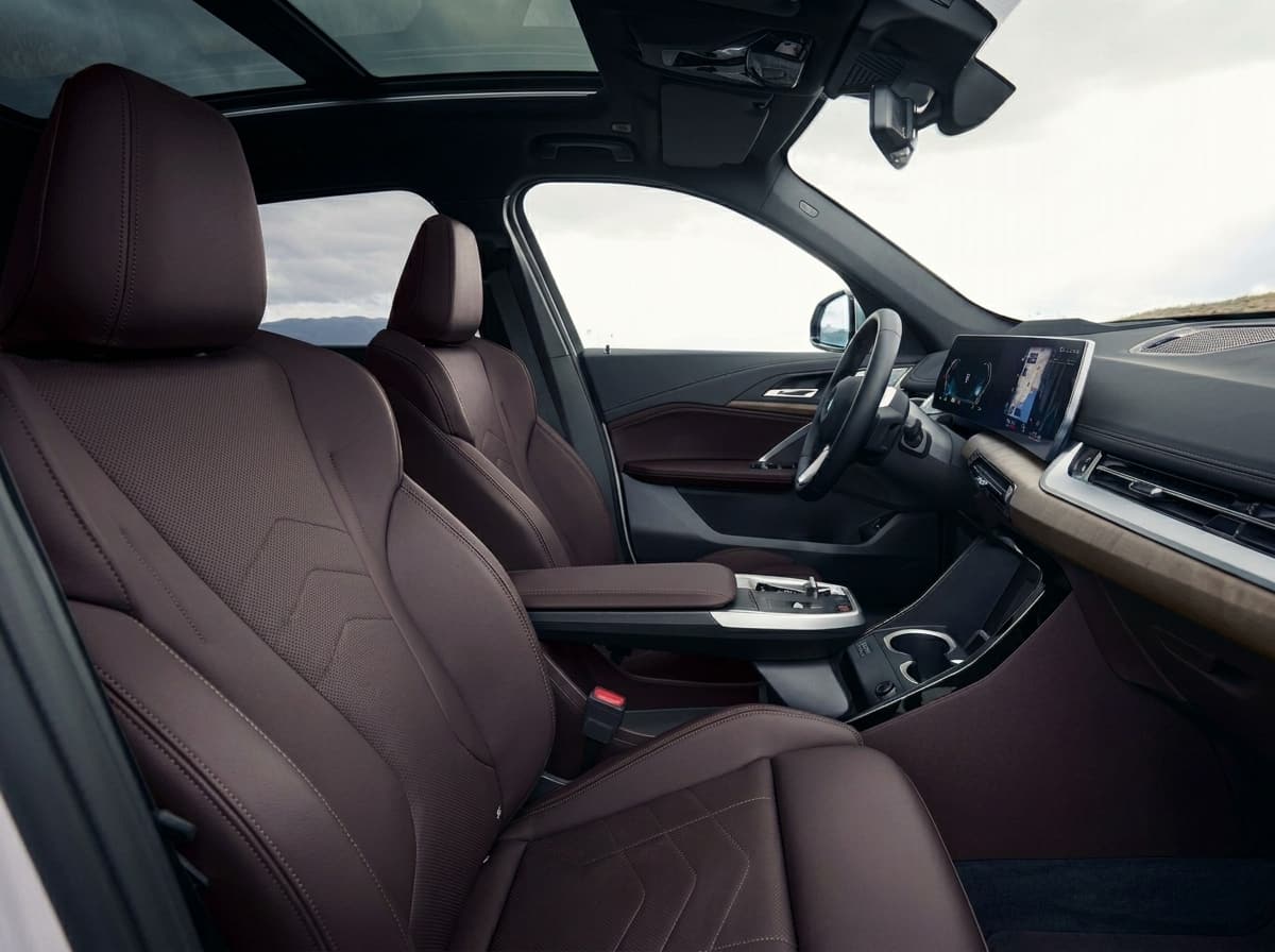 BMW X1 front seats and panoramic roof seen from the open passenger door, hills outside